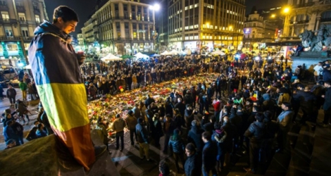 Un homme enveloppé dans un drapeau belge tient une bougie place de la Bourse, à Bruxelles, le 24 mars 2016, en hommage aux victimes des attentats de l'aéroport de Zaventem et du métro bruxellois.