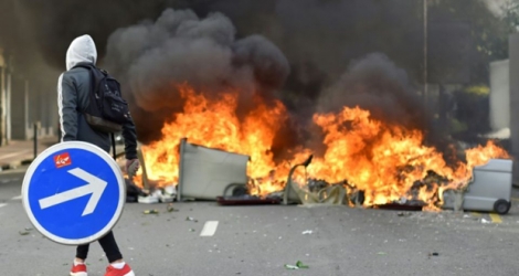Le 31 mars à Nantes, un homme transporte un panneau de signalisation en passant devant des poubelles en feu.
