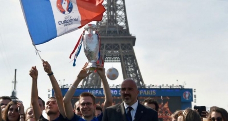 Un supporter tient le drapeau de l'Euro-2016 dans la fan zone au pied de la Tour Eiffel à Paris, tandis que des milliers de personnes se rassemblent pour le concert, le 9 juin 2016