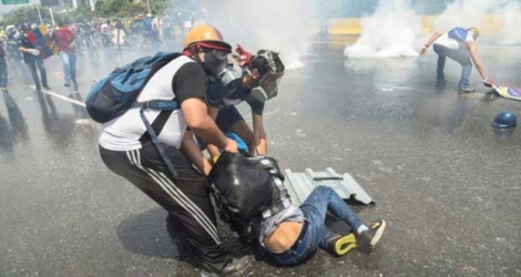 Un manifestant aidé par d'autres manifestants après avoir été aspergé par des canons à eau de la police lors d'une marche à Caracas le 10 mai 2017 