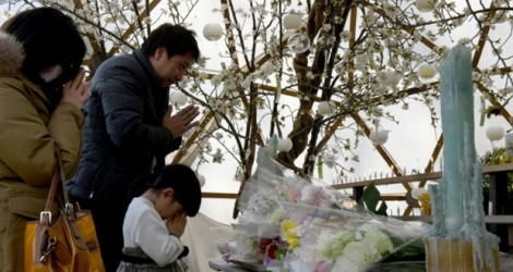Une famille prie pour les victimes du tremblement de terre et du tsunami de mars 2011 dans le nord-est du Japon, sept ans après, le 11 mars 2018, dans un parc de Tokyo.