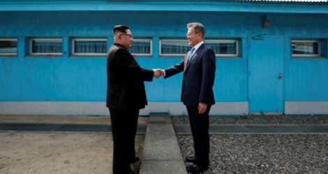 Moon Jae-in (d) et Kim Jong Un se serrent la main sur la ligne de démarcation avant le début du sommet, le 27 avril 2018 à Panmunjom.