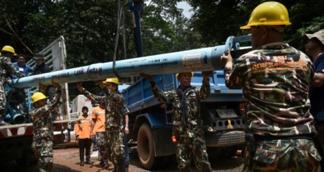 Des techiciens transportent des tuyaux de pompage près de la grotte de Tham Luang où sont piégés douze enfants et leur entraîneur de football, le 1er juillet 2018 à Chiang Rai, en Thaïlande.
