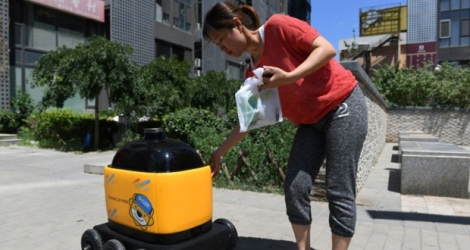 Une femme récupère ses provisions acheminées par un robot livreur au cours d'une démonstration à Pékin, le 28 juin 2018 