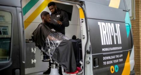 Kris Robertson coupe les cheveux d'un client à bord de la fourgonnette abritant un petit salon de coiffure, le 17 mai 2019 à Londres.