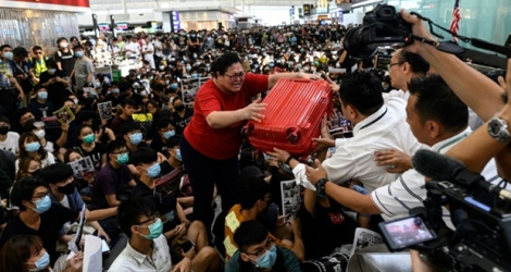 Une touriste tente de confier sa valise à des gardes de sécurité pour gagner la zone d'embarquement durant une nouvelle manifestation pro-démocratie à l'aéroport international de Hong Kong le 13 août 2019.