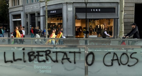 Des jeunes drapés dans des drapeaux catalans passent devant un graffiti «Liberté ou Chaos» après une nouvelle nuit de violences, le 18 octobre 2019 à Barcelone.