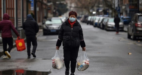 Une femme, un masque de protection sur le visage, porte des sacs de provision dans une rue de Wuhan, le 26 janvier 2020 en Chine.