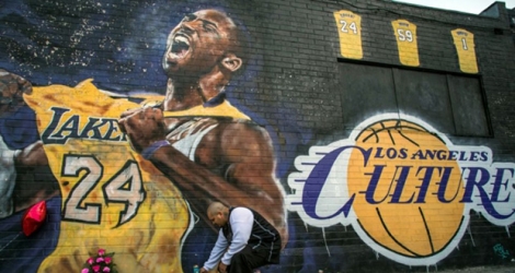 Un homme alume une bougie devant une fresque murale représentant Kobe Bryant à Los Angeles, le 26 janvier 2020, peu après l'annonce de la mort accidentelle de l'ancien joueur de basket.