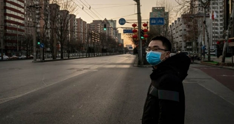 Un homme avec un masque s'apprête à tyraverser une artère de Pékin, désertée, le 31 janvier 2020.