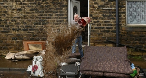 Un homme vide un seau d'eau devant sa maison à Mytholmroyd, dans le nord de l'Angleterre, le 10 février 2020 après les inondations provoquées par le passage de la tempête Ciara.