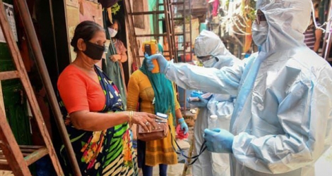Des soignants en combinaison de protection font du porte-à-porte pour contrôler la température des habitants du bidonville de Dharavi, le 24 juin 2020 à Bombay, en Inde.