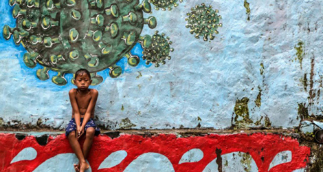Un jeune garçon est assis devant une fresque murale représentant le coronavirus à Bogor, dans l'ouest de l'île de Java, en Indonésie, le 27 septembre 2020.