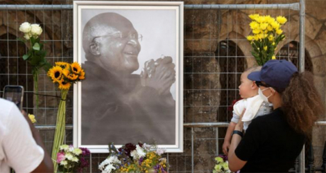 Des personnes déposent des fleurs auprès de l'effigie de Desmond Tutu accrochée devant la cathédrale Saint-Georges au Cap, le 26 décembre 2021.