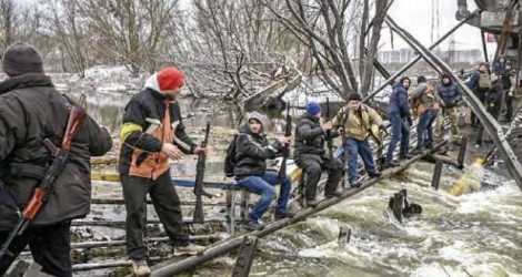 Des membres de l’unité de défense civile ukrainienne font passer des fusils de l’autre côté d’un pont détruit à Kiev, hier.