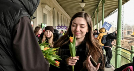 Une jeune femme sourit en recevant une tulipe offerte par un prêtre à l'occasion de la journée des droits des femmes, dans la gare de Przemyl (Pologne), où des centaines de réfugiés ukrainiens attendent une solution de relogement, le 8 mars 2022.