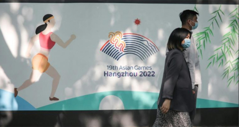 Deux piétons passent devant le logo des Jeux asiatiques, le 8 mai 2022 à Hangzhou, prévus initialement du 10 au 25 septembre, mais reportés pour cause d'épidémie de Covid 19, du 23 septembre au 8 octobre 2023.